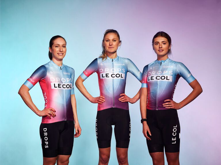 Drie vrouwen van het Drops Le Col wielrenteam in hun sportkleding. 